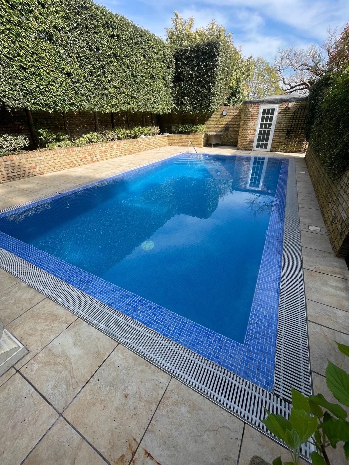 Outdoor pool with blue mosaic tiling and a grille overflow edge