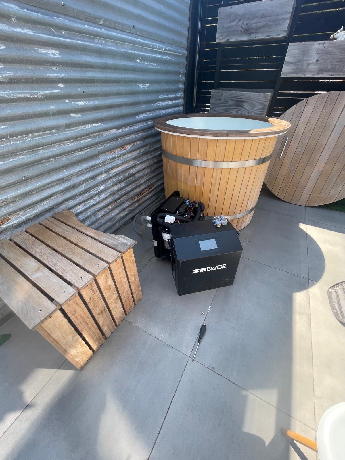 Wooden cold plunge tub with a chiller unit beside a sauna bench