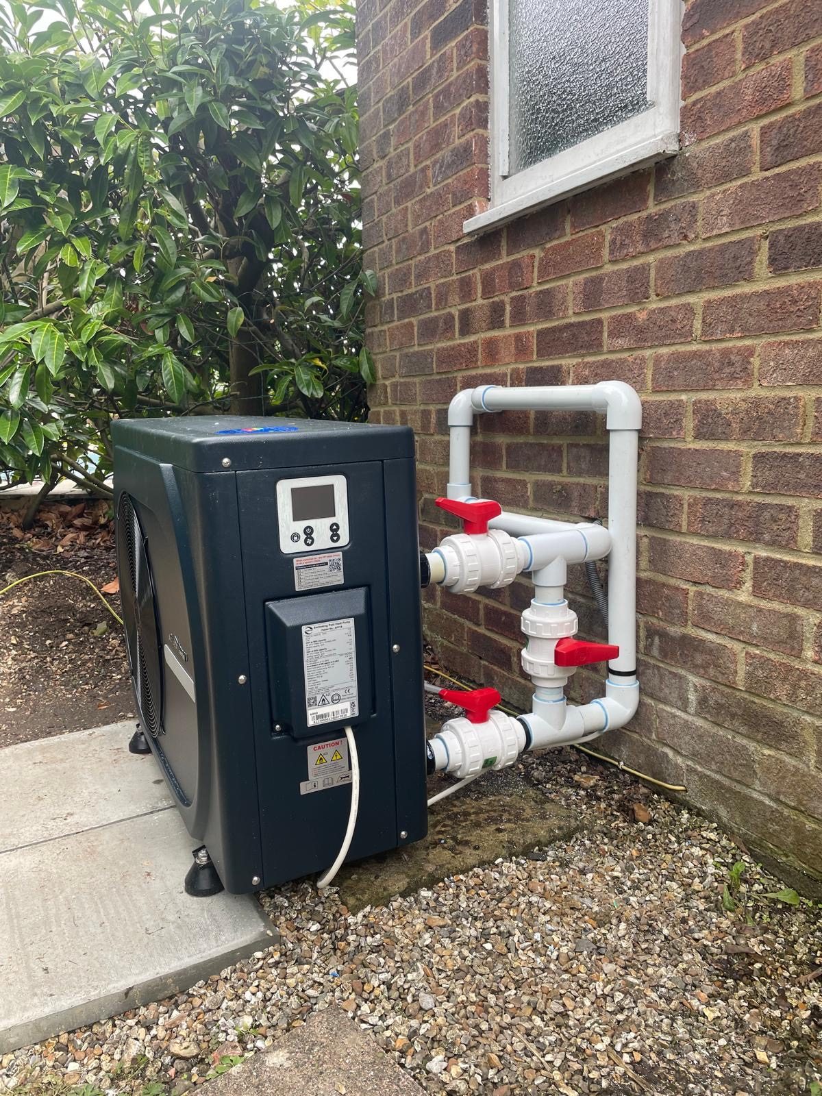 Pool heat pump installed against a house wall with new pipework