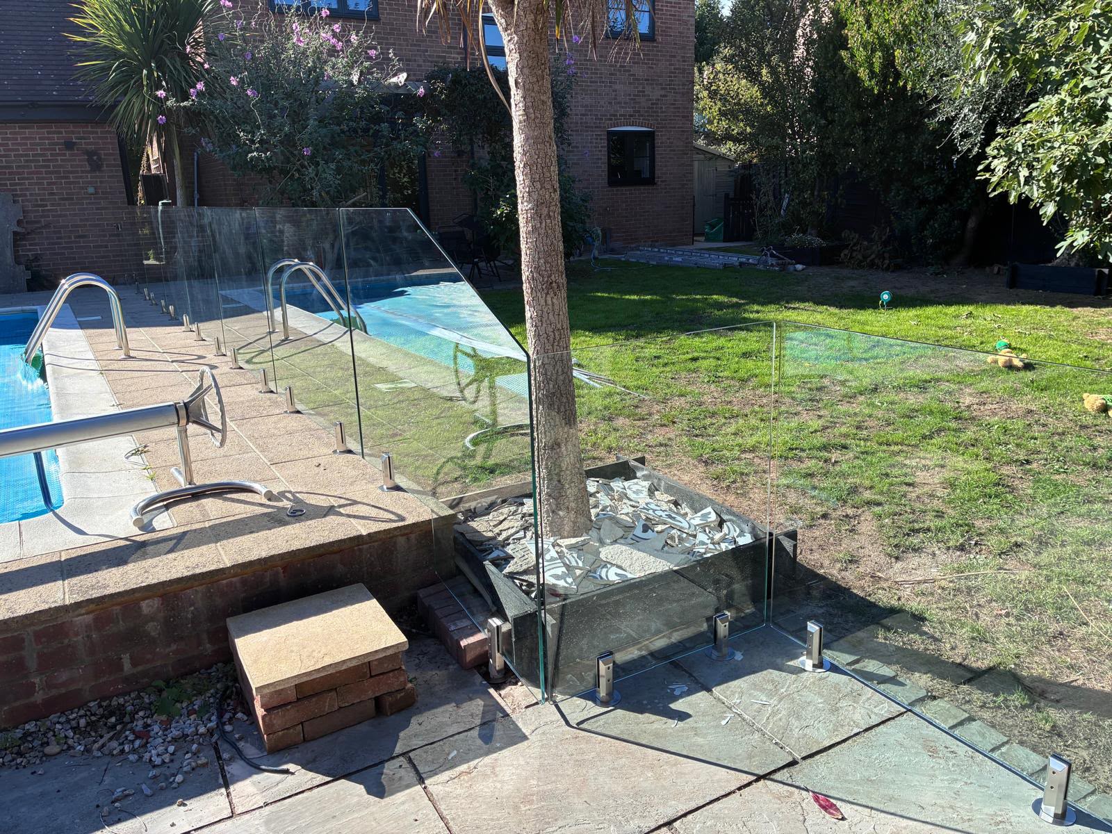 Frameless glass fence returned around a poolside tree and raised planting bed