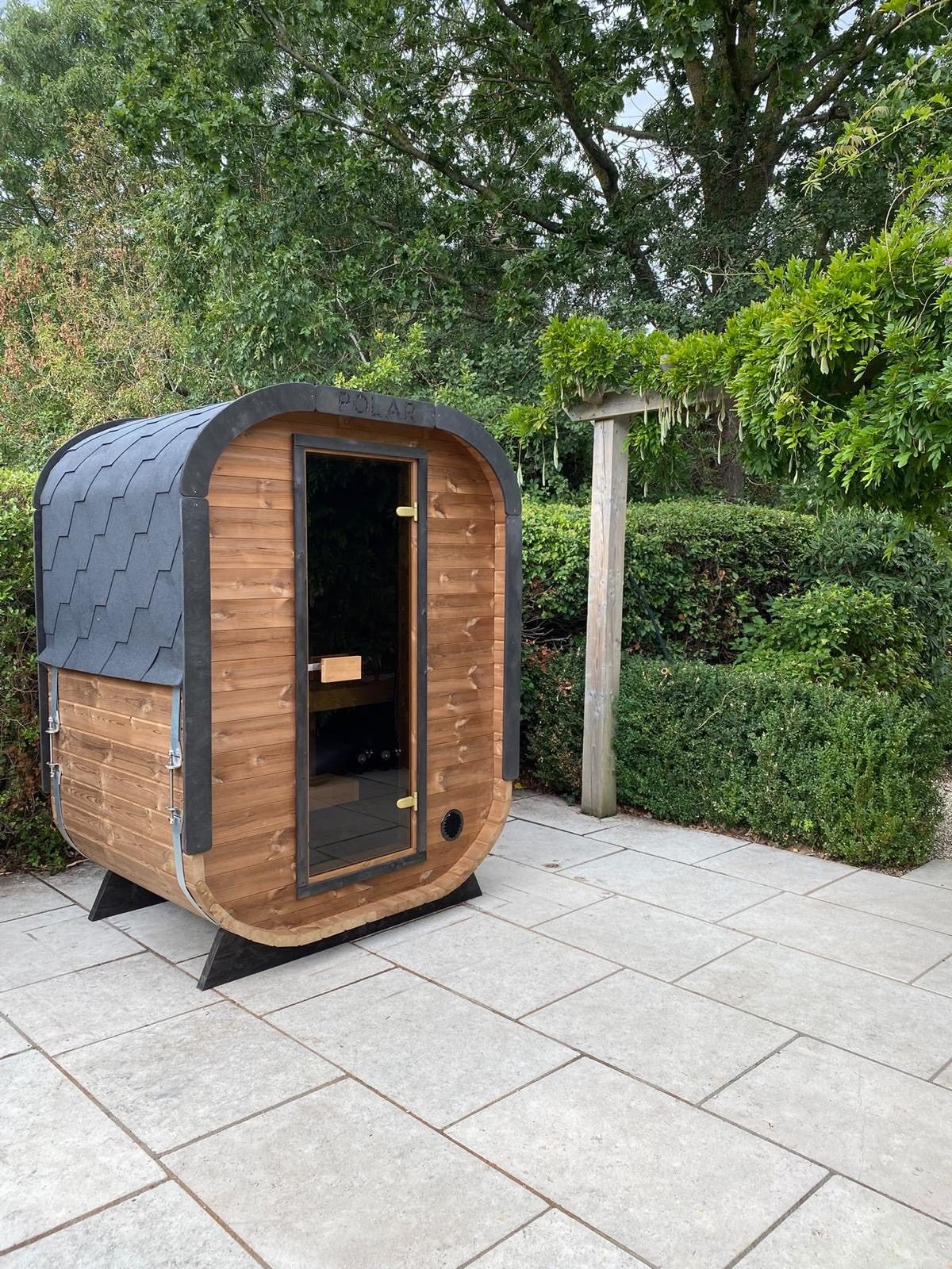 Outdoor timber sauna cabin with a glass door on a paved patio