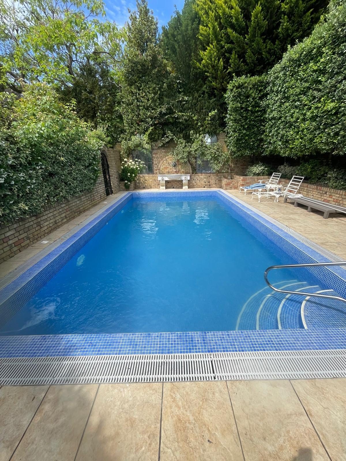Outdoor pool with a grille overflow edge and hedged garden