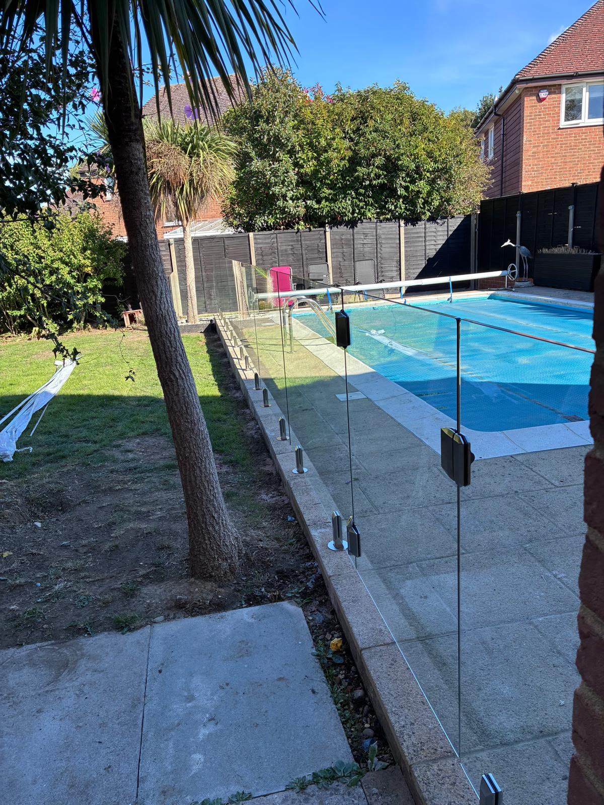 Glass pool fencing running along a lawn beside a rectangular swimming pool