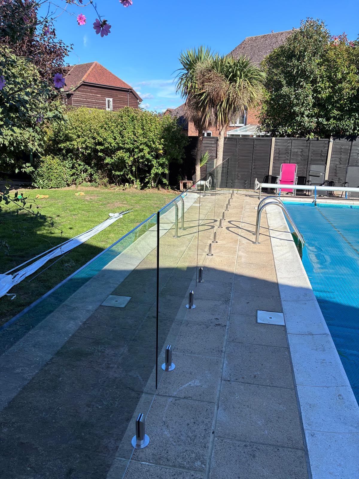 Frameless glass pool fencing along a paved poolside with stainless steel spigots